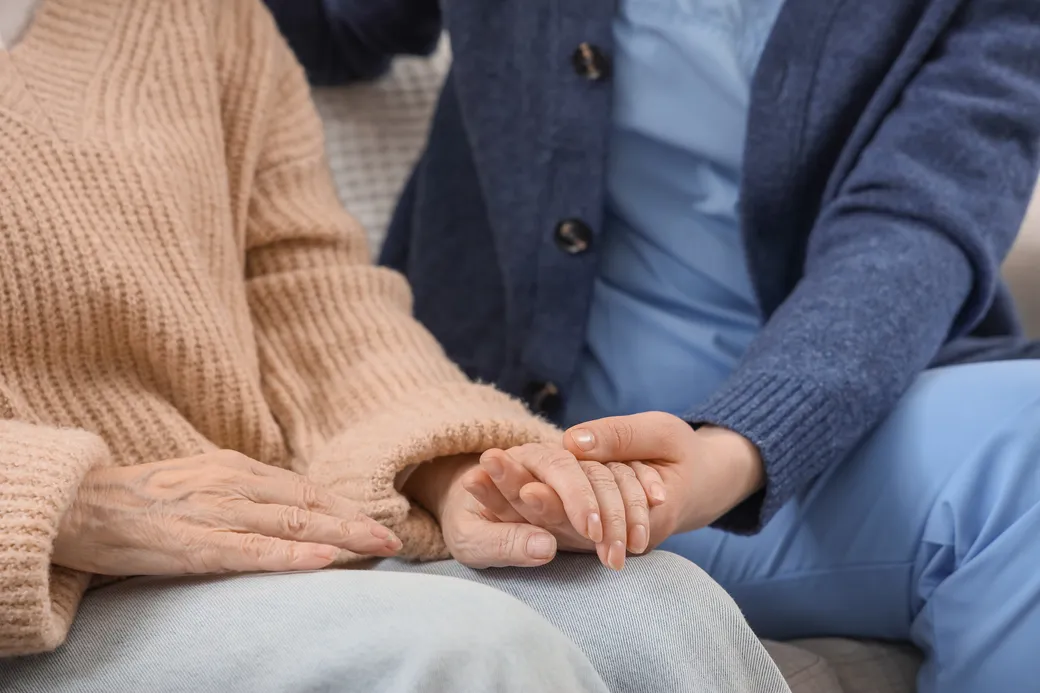A caregiver holding a resident's hand on a sofa at home
